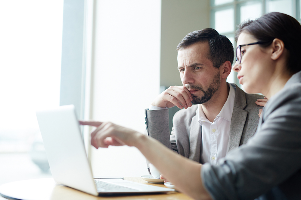 Two analysts discussing online data in front of laptop